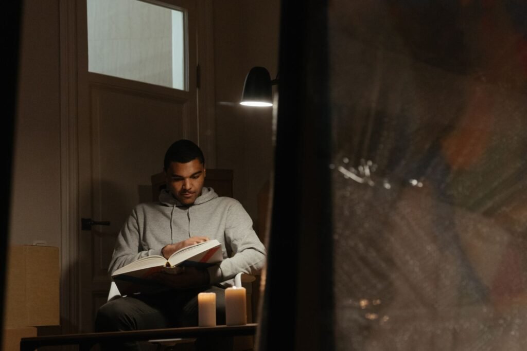 Man reading a book by lamplight and candles as part of a calming evening routine