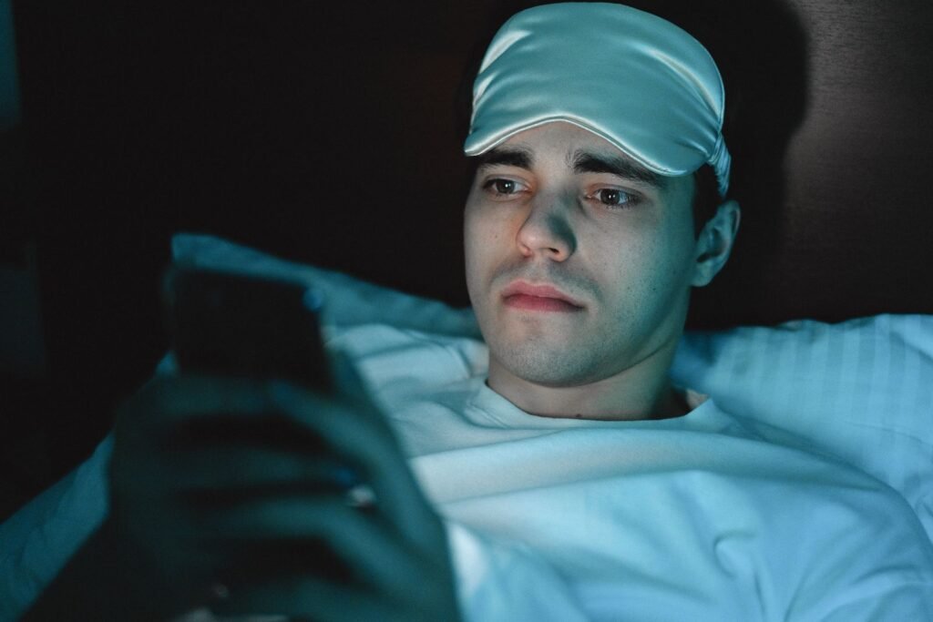 Tired man lying in bed at night staring at his phone screen, feeling wired but tired
