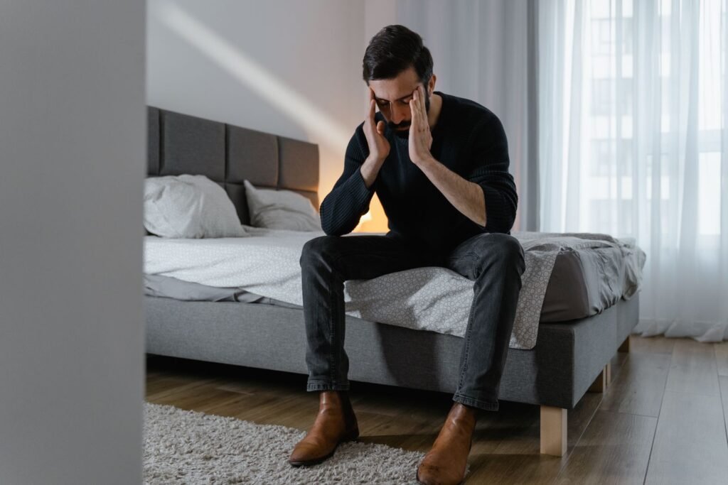 Stressed man sitting on his bed holding his head, showing signs of high cortisol at night